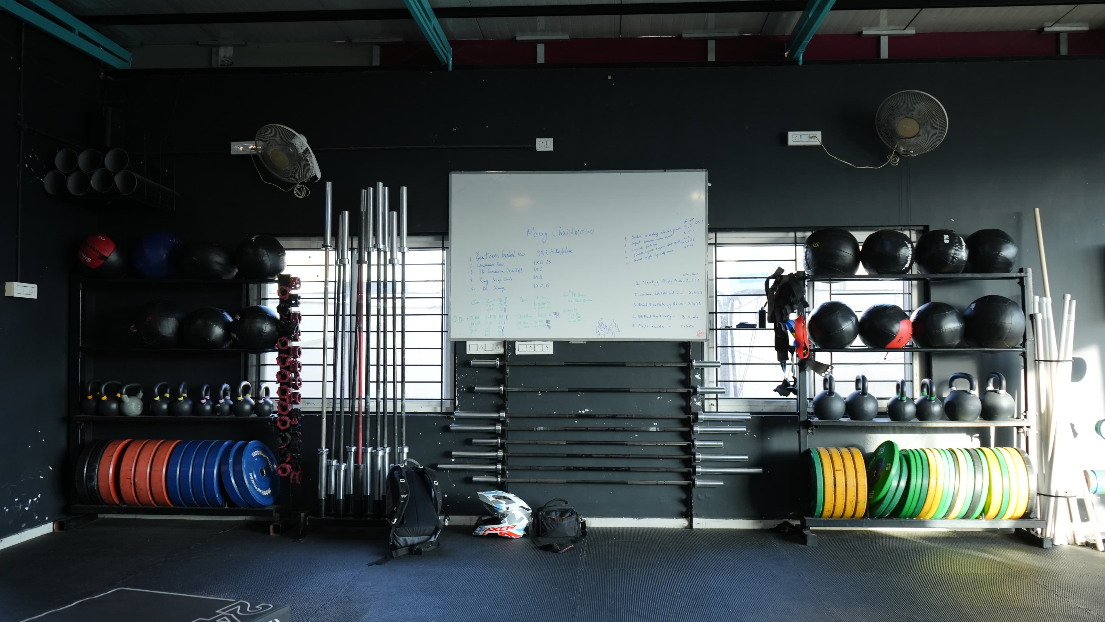Olympic barbells and bumper plates at Xthrive HSR Layout, with the daily strength and conditioning programming whiteboard.