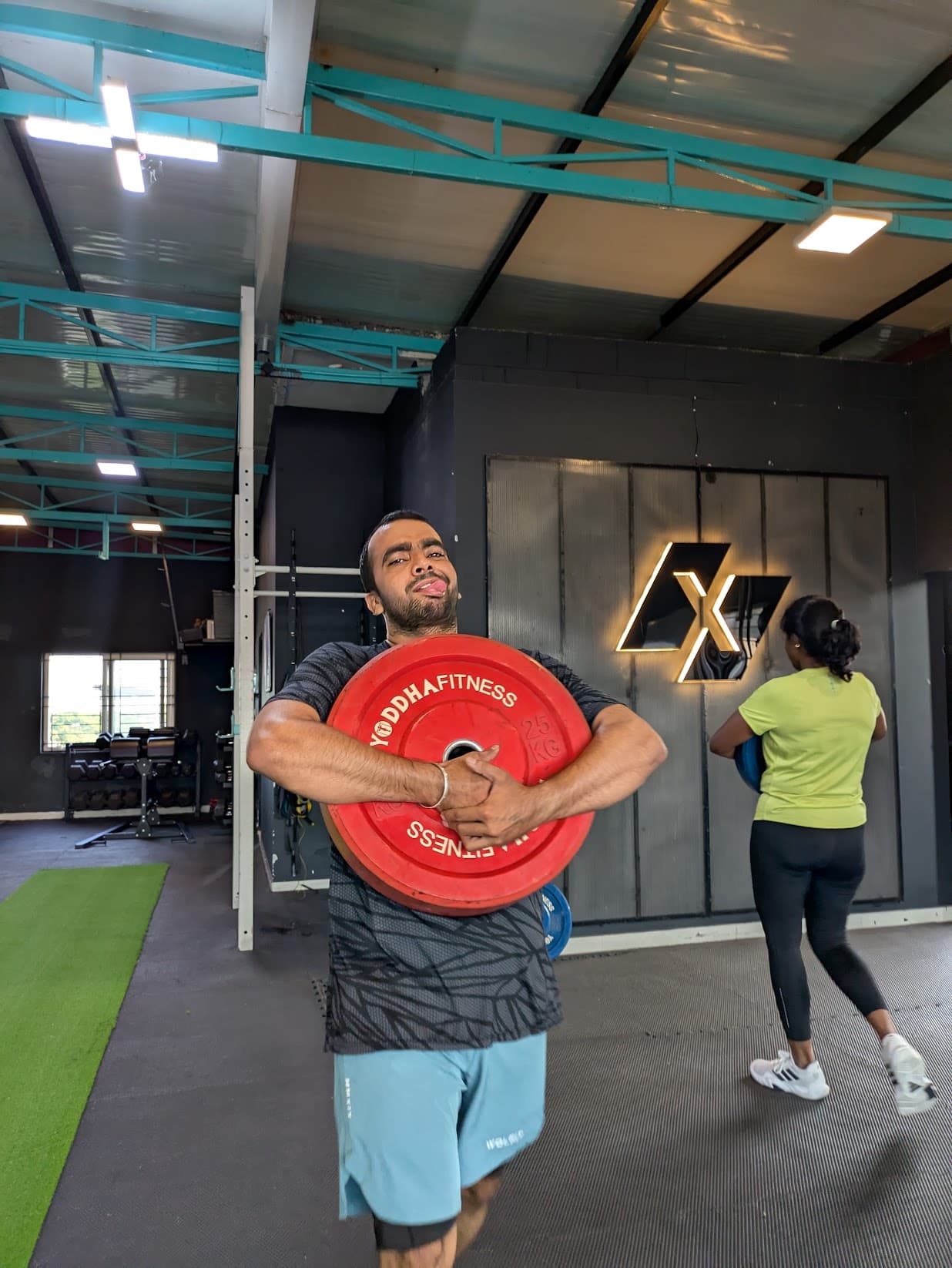 Member training with bumper plates beside the Xthrive logo wall at the HSR Layout gym in Bengaluru.